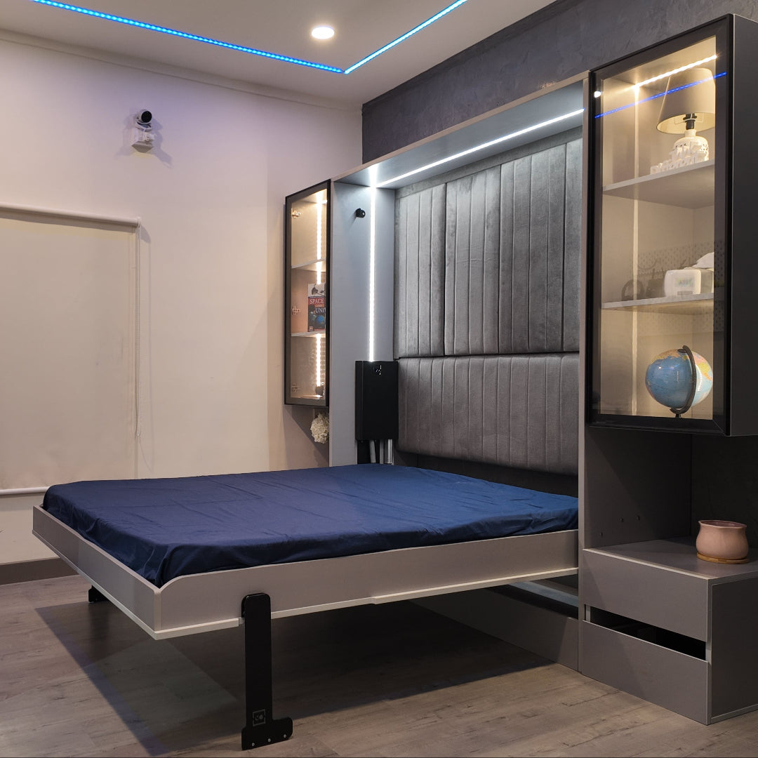 A modern bedroom featuring an electric invisible bed with blue bedding, alongside built-in shelving units with various decorative items. The bed is lowered and extended into the room, showcasing a sleek, space-saving design.