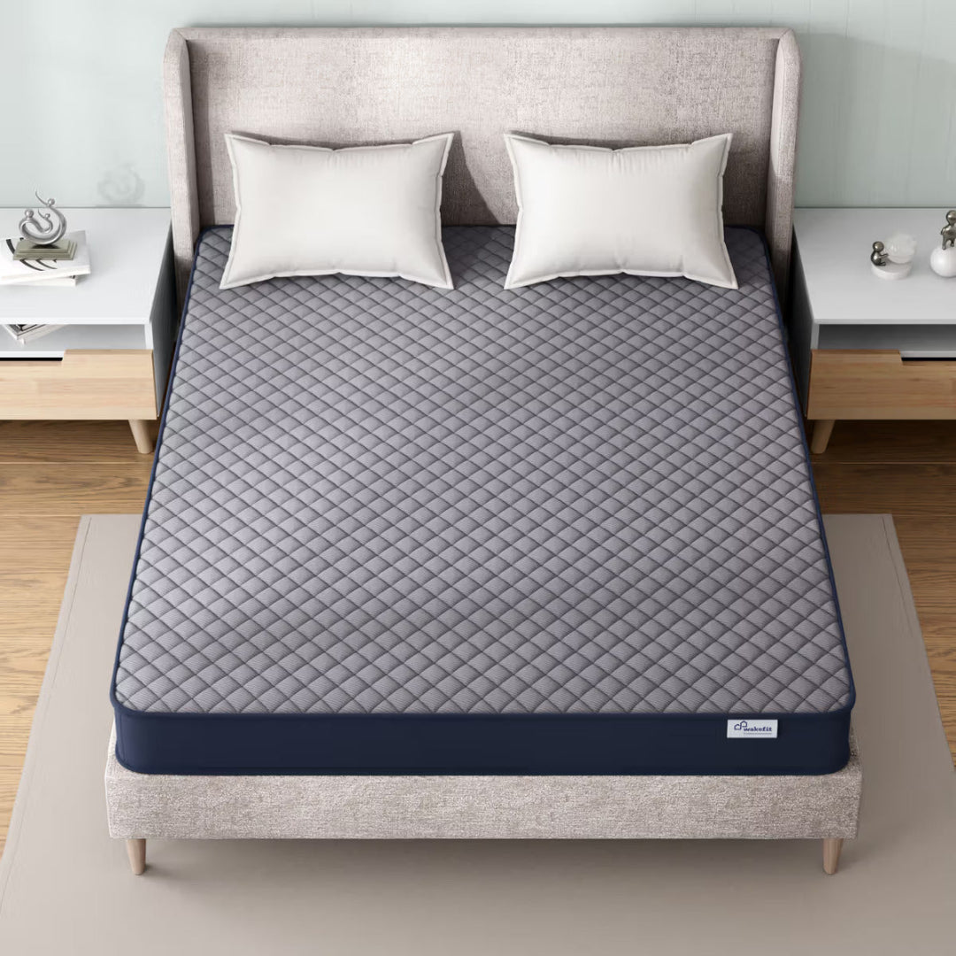 Gray quilted mattress cover on a bed with white pillows in a bedroom setting.